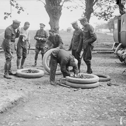 Truppe britanniche che cambiano pneumatici su uno dei veicoli utilizzati durante la visita di Alberto I, re dei Belgi, al fronte occidentale, Villers Carbonnel, il 17 maggio 1917. © IWM (Q 2206)
