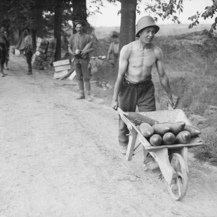 Un soldato britannico, che indossa un elmetto tedesco,  spinge una carriola con proiettili di artiglieria in un carriola durante la battaglia di Messines, l'8 giugno 1917.© IWM (Q 2283)