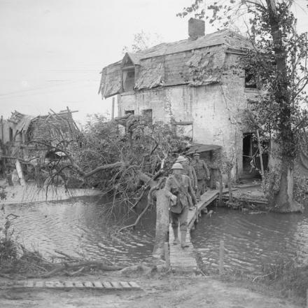 Soldati che attraversano un ponticello di tavole su un piccolo ruscello tra case danneggiate. Vicino a Boezinge, il 28 agosto 1917. © IWM (Q 5928)