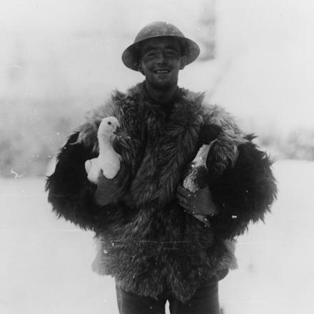 Un soldato del Machine Gun Corp in un cappotto di pelle di pecora con due anatre per il suo pranzo di Natale, vicino a Hesdin, il 20 dicembre 1917. © IWM (Q 8355)