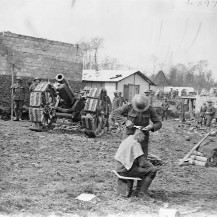 Un obice da 6 pollici della Royal Garrison Artillery in posizione a Ransart, 7 aprile 1918. In primo piano, il barbiere della batteria sta tagliando i capelli di uno degli artiglieri. © IWM (Q 8676)