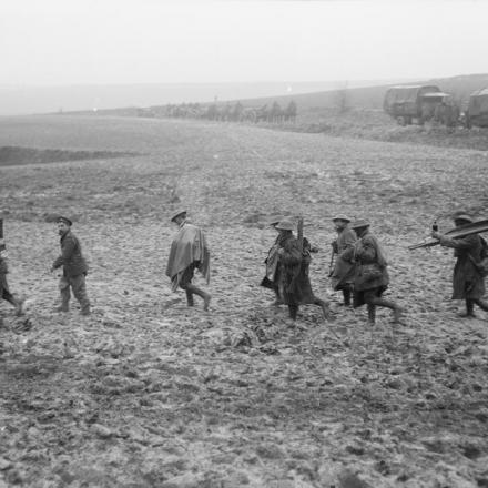 Truppe, tra cui un soldato che trasporta una barella, risalgono le linee attraverso un'area fangosa, 58th (London) Division, vicino a Domart, 8 aprile 1918. © IWM (Q 10873)