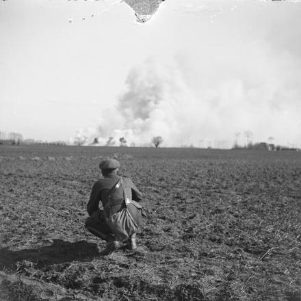 Battaglie del Lys. Un soldato che osserva un deposito di munizioni lontane che brucia vicino a Robecq, aprile 1918. © IWM (Q 6522)