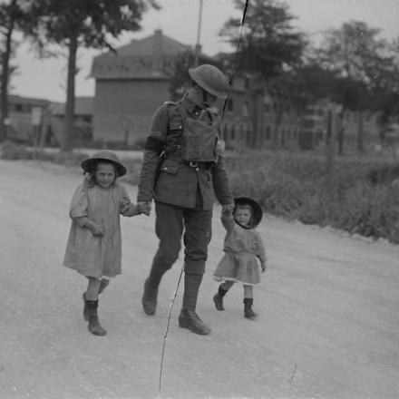 © IWM Un poliziotto militare che cammina con due piccole ragazze francesi che indossano elmi d'acciaio. Bethune, 14 maggio 1918 