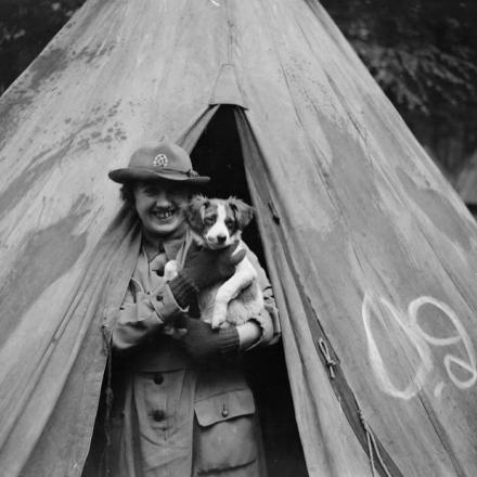 Un membro del Queen Mary's Army Auxiliary Corps sbuca da una tenda con un cane in braccio nella foresta di Crecy, il 7 giugno 1918. © IWM (Q 11067)