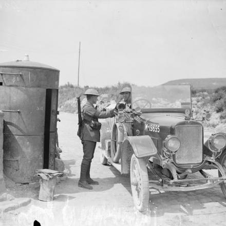 Un controllore del traffico, con indosso il suo bracciale, esamina il lasciapassare di un autista a Souchez.  La casetta di sentinella è blindata da usare durante i bombardamenti. 13 giugno 1918. © IWM (Q 6733)