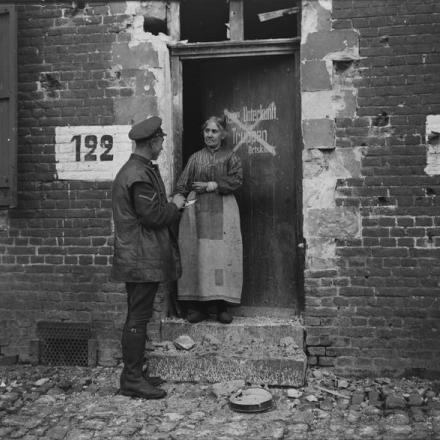 Un caporale inglese parla con una donna francese sulla porta della sua casa danneggiata a Bouchain, il 25 ottobre 1918. Un cartello in tedesco sulla porta, ora cancellato, dice "No Lodging For Troops". © IWM (Q 3318)