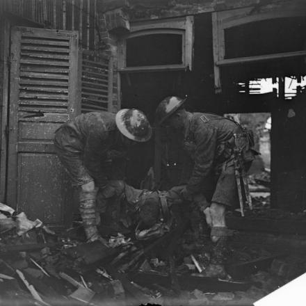 Due uomini del 18 ° Battaglione, il London Regiment (London Irish Rifles), che portano in una casa una vittima durante la ronda diurna ad Albert, il 6 agosto 1918.© IWM (Q 6904)
