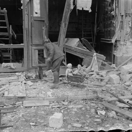 La facciata di un negozio in rovina, per i  danni causati da mine tedesche ad azione ritardata. Cambrai, 11 ottobre 1918. Un soldato britannico  indossa un elmetto chiodato come trofeo. © IWM (Q 11807)