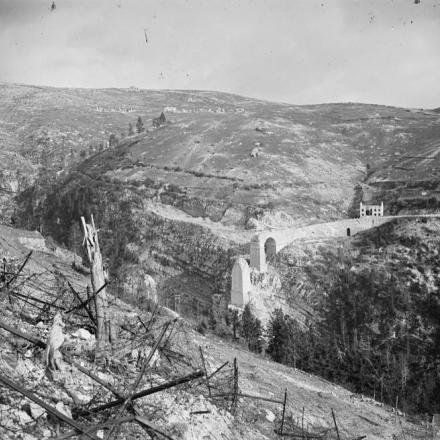 Vista della strada di montagna della Val d'Assa che mostra un ponte distrutto e le difese del filo spinato austro-ungariche distrutte.