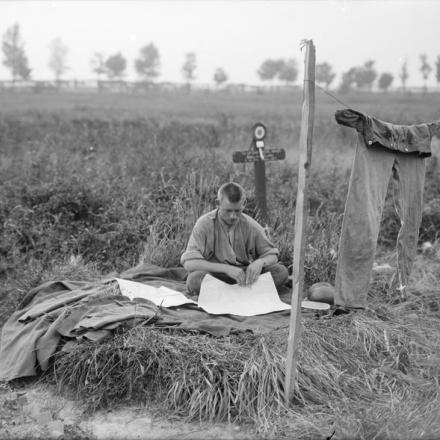 Un soldato belga seduto a terra vicino a una tomba di guerra, mentre si asciuga i vestiti a Ramscapelle, il 9 settembre 1917. © IWM (Q 2959)