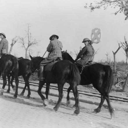 Uomini a cavallo su una strada vicino a Ypres, il 6 settembre 1917. Uno, un australiano, porta una croce per una tomba di guerra. © IWM (Q 3004)