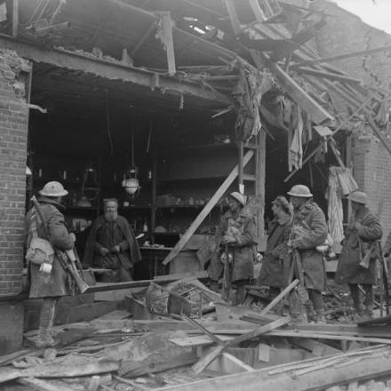 Soldati britannici fuori da un negozio quasi completamente distrutto ad Amiens, il 3 aprile 1918. Il proprietario è seduto in attesa di clienti. © IWM (Q 10856)