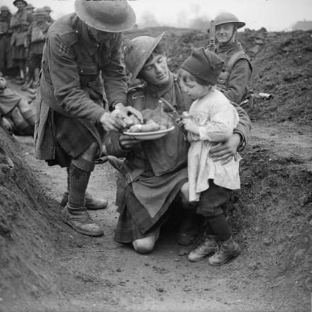 Uomini del 4 ° Battaglione, Gordon Highlanders (51ª Divisione) che danno da mangiare a una bambina rifugiata nella loro trincea improvvisata vicino a Locon, il 10 aprile 1918. © IWM (Q 7855)