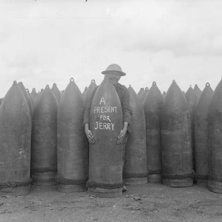 Un soldato britannico posa con una granata pesante con un messaggio scritto con il gesso "Un regalo per Jerry" in un deposito di granate, il 27 agosto 1918. © IWM (Q 11260)